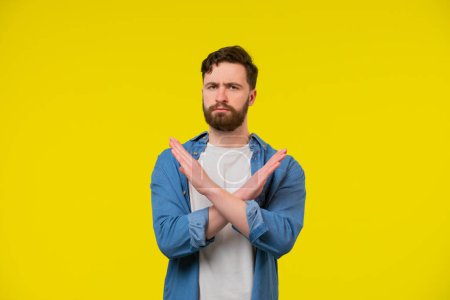 Photo for Portrait of young handsome man showing disagreement by doing x crossed hand gesture in isolated studio yellow background - Royalty Free Image