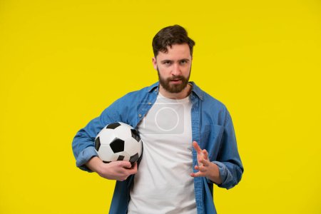 Photo for Excited young bearded man football fan in white t-shirt cheer up support favorite team with soccer ball screaming clenching fist isolated on yellow background. People sport family leisure concept. - Royalty Free Image