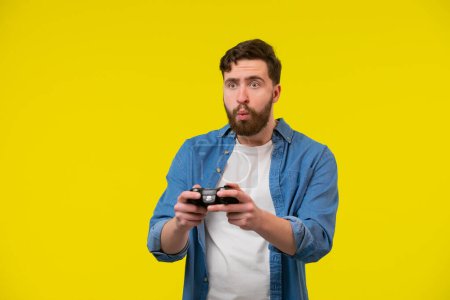Foto de De cerca la foto de miedo nervioso fan de los videojuegos, él está sosteniendo una consola, aislado sobre fondo amarillo brillante, espacio de copia - Imagen libre de derechos
