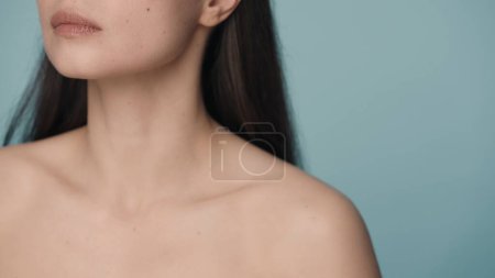 Téléchargez les photos : Menton parfait, cou élancé et épaules nues d'une femme sur un fond bleu rapproché. Soins de la peau, soins du corps, cosmétologie, chirurgie plastique - en image libre de droit