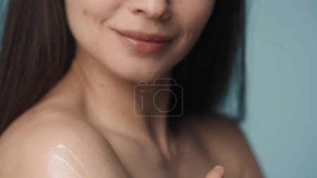 Photo for With slow massage movements, the woman applies the cream on her shoulder. A seminude woman takes care of her skin close up on a blurred blue background. The concept of skin and body care. Natural - Royalty Free Image