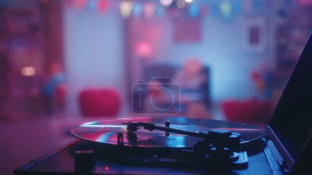 Téléchargez les photos : Jouer un disque vinyle sur une platine vintage close-up sur un fond flou d'une pièce décorée pour une fête. L'intérieur de la chambre est décoré d'un miroir boule disco, drapeaux, ballons - en image libre de droit
