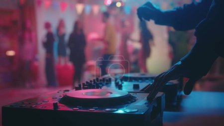 Male hands mix music on a dj console against a blurred background of dancing people. The concept of a holiday, celebration, disco