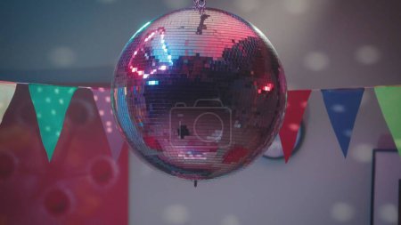 A silvery mirrored disco ball casts multi-colored reflections on the walls close up. Party with disco ball and paper flags. Party, birthday, holiday, disco