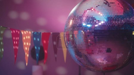 Téléchargez les photos : La boule de disco miroir fascine par ses rayons multicolores lumineux. Boule disco près sur le fond de la pièce. Fond musical et de danse de la soirée - en image libre de droit
