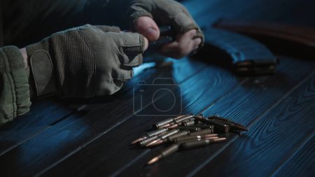 Foto de Un soldado descarga el cargador de un rifle de asalto Kalashnikov, colocando cartuchos sobre una mesa de madera. Un primer plano de las manos de un soldado ucraniano quitando cartuchos de los cargadores de armas pequeñas - Imagen libre de derechos