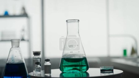 Foto de Experimento científico. Un frasco Erlenmeyer con un líquido verde sobre la mesa sobre un fondo borroso de laboratorio - Imagen libre de derechos