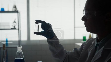Foto de Investigación y desarrollo de una vacuna. Silueta oscura de una científica con un frasco de ampolla de vidrio de cerca. Concepto: enfermedad, atención médica, ciencia, anestesia - Imagen libre de derechos