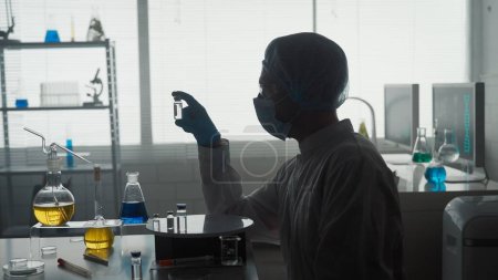 Foto de Investigación y desarrollo de una vacuna. Silueta oscura de un científico varón con un frasco de ampolla de vidrio. Concepto: enfermedad, atención médica, ciencia, anestesia - Imagen libre de derechos