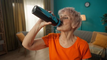 Téléchargez les photos : Une femme âgée fatiguée boit de l'eau après l'exercice. Le concept de style de vie sportif, retraite, santé, bien-être - en image libre de droit