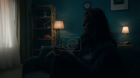 Foto de Mujer joven devastada, desapegada y solitaria se sienta en un sofá en una habitación oscura de cerca. Mujer desesperadamente pensando en problemas personales, pasando por una crisis. Desesperanza. El concepto de salud mental - Imagen libre de derechos