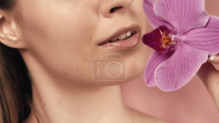 Photo for Female lips with delicate pink lipstick and orchid flower closeup on a pink blurred background. A beautiful smile. Perfect female face makeup. Lipstick. The concept of beauty, cosmetology, skin care - Royalty Free Image