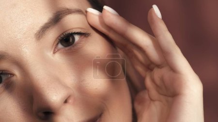 Schnappschuss eines Frauengesichts im Studio auf rosa Hintergrund in Großaufnahme. Eine Frau berührt mit der Hand ihre Augenbrauen. Gute Sicht und Augenpflege. Kontaktlinsen. Natürliche weibliche Schönheit. Kosmetische Linie