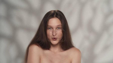 Téléchargez les photos : Portrait d'un beau jeune modèle caucasien. Gros plan d'une fille aux cheveux longs, aux yeux bleus et au maquillage nu regardant la caméra de façon ludique. Concept de publicité beauté. - en image libre de droit
