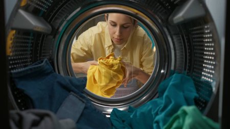 Mujer adulta en ropa casual con cesta de la ropa abre la puerta de la lavadora y saca la ropa fresca. Vista desde el interior de la lavadora.