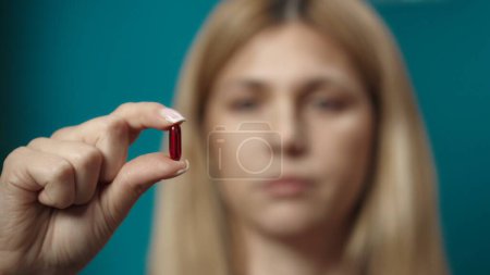 Photo for Portrait of caucasian blonde woman. Close up shot of female model holding a red capsule pill in her hand. Home medicine concept. Healthcare advertisement. - Royalty Free Image