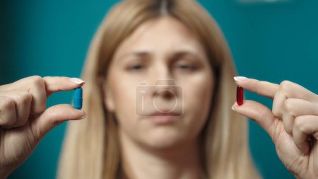 Photo for Close up shot of female blonde model holding a blue and red capsules in her hands and looking at the. Home medicine concept. Healthcare advertisement. - Royalty Free Image