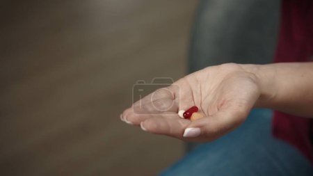 Photo for Close up shot of a female model sitting on the sofa with a handful of colorful pills, showing her hand to the camera. Healthcare concept advertisement. - Royalty Free Image