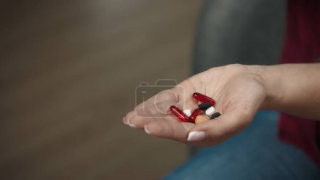 Photo for Close up shot of a female model sitting on the couch with a handful of colorful pills, showing her open hand to the camera. Healthcare concept advertisement. - Royalty Free Image