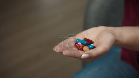 Photo for Close up shot of a female model sitting on the couch with a handful of colorful pills and capsules, showing her hand to the camera. Healthcare concept advertisement. - Royalty Free Image