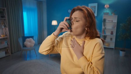 Téléchargez les photos : Une femme utilise un inhalateur d'asthme dans le salon à la maison de près. Lutte contre les allergies, l'asthme. Concept de médecine familiale - en image libre de droit
