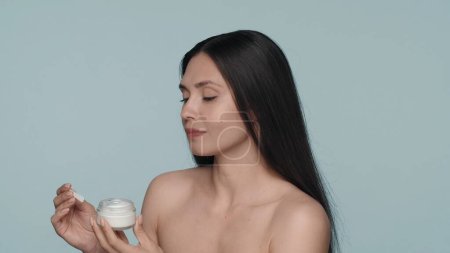 Photo for Cream for skin care. A young seminude woman holds a jar of face or body cream in the studio on a blue background close up. The concept of beauty, cosmetology, skin care - Royalty Free Image