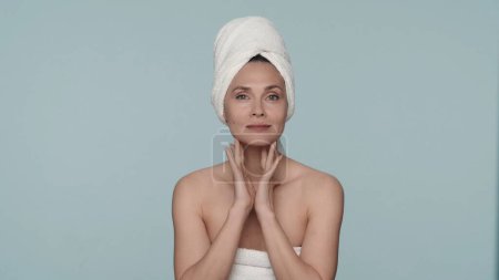 Téléchargez les photos : Portrait d'une femme enveloppée dans des serviettes de bain dans le studio sur un fond bleu de près. Une femme jouit de sa peau lisse et propre après une douche. Le concept de beauté, cosmétologie, soin de la peau - en image libre de droit
