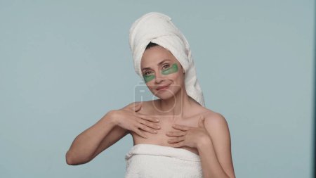 Téléchargez les photos : Une femme enveloppée dans des serviettes de bain après la douche, avec des patchs sur fond bleu. Une femme bénéficiant de l'effet cosmétique d'un savon hydratant, gel, lotion. Le concept de beauté, de cosmétologie, de peau - en image libre de droit