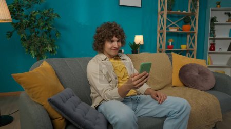 Foto de Retrato de primer plano de un joven modelo masculino con ropa casual sentado en el sofá de la sala de estar y hablando - Imagen libre de derechos