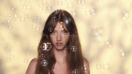 Photo for Close up shot of a attractive female model with long hair. Girl looks at the camera and many soap bubbles flying around her. Skincare advertisement concept. - Royalty Free Image