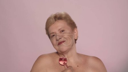 Foto de Retrato de una mujer mayor. Primer plano de una modelo femenina de mediana edad haciendo un masaje con globos de cristal de criosfera rosa en el pecho y la zona de la clavícula. Belleza cuidado de la piel concepto de publicidad. - Imagen libre de derechos