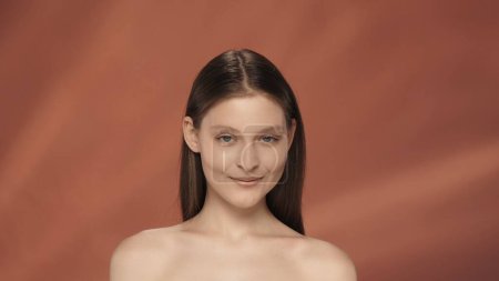 Téléchargez les photos : Portrait d'une jeune séminude souriante en studio sur fond rouge en gros plan. Le concept de beauté naturelle, cosmétologie, soins de la peau - en image libre de droit