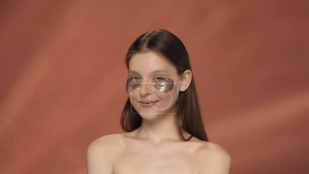 Téléchargez les photos : Portrait d'une femme avec des taches d'hydrogel sous les yeux de près. Une femme en studio sur fond rouge. Le concept de beauté, de cosmétologie - en image libre de droit