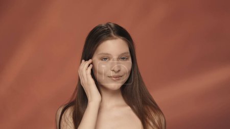 Foto de Retrato de una joven seminud sonriente en el estudio sobre un fondo rojo de cerca. El concepto de belleza natural, cosmetología, cuidado de la piel - Imagen libre de derechos