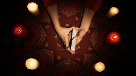 Photo for Fortune teller session scene. Close up shot of female hands holding tarot cards, surrounded by candles on the table. Woman preparing for divination. - Royalty Free Image