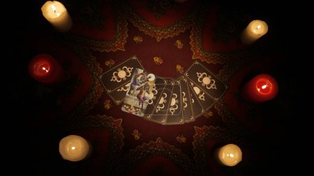 Photo for Close up shot of a table with ethnic tablecloth and a fan of tarot cards laying on one card is laying on top open. Candles standing around. Space to insert an advertisement. - Royalty Free Image