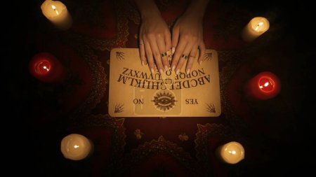 Photo for Magical session scene, top view. Close up shot female hands moving over spirit board trying to speak with ghosts using ouija game. Occult divination concept. - Royalty Free Image