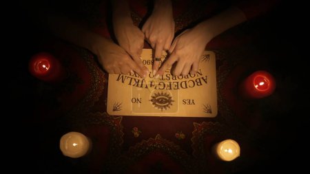 Photo for Magical scene, top view. Close up shot of people hands moving over the spirit board. People reading the message from ghosts using an ouija game. Occult divination concept. - Royalty Free Image