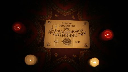 Photo for Magical session scene. Close up shot of spiritual board game with alphabet on the table, many lighted candles standing around. Occult divination concept. - Royalty Free Image