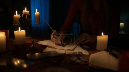 Photo for Close up shot of table with many candles and tarot cards laying around. woman writes something with feather pen on the old paper. Magical aesthetic concept. - Royalty Free Image