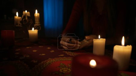 Photo for Close up shot of the table in the room with candlelight. Woman holding a deck of tarot cards, preparing to make a layout. Divination concept. - Royalty Free Image