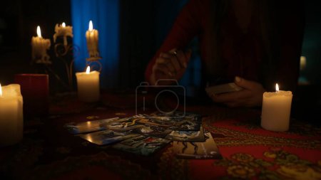 Photo for Close up shot of the table in the room. Woman takes out cards from the deck and lays them on the table, making a tarot layout for herself. Divination concept. - Royalty Free Image