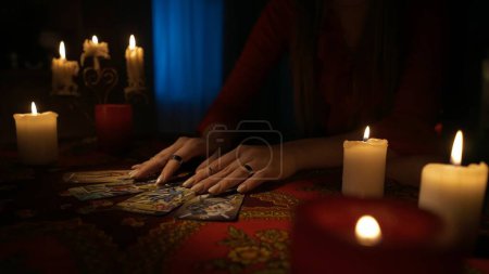 Photo for Close up shot of the table in the dark room. Woman takes out cards from the deck and place them on the table, making a tarot layout for herself. Divination concept. - Royalty Free Image