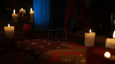 Photo for Close up shot of the table in the room with many candles standing around. Woman model takes away the tarot cards, finishing her layout. Divination concept. - Royalty Free Image