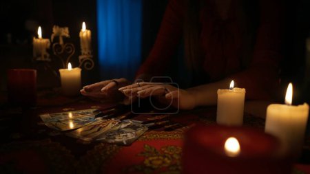 Photo for Close up shot of the table in the room with candlelight. Woman holding hands over the layout of tarot cards she made for herself. Divination concept. - Royalty Free Image