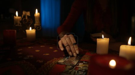 Photo for Close up shot of the table in the room with many candles around. Woman model placing out tarot cards from the deck, making a destiny layout. Divination concept. - Royalty Free Image