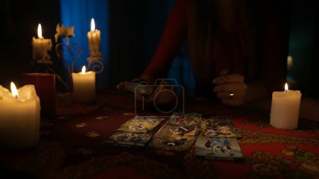 Photo for Close up shot of the table in the dark room with many candles around. Woman taking out tarot cards from the deck on the table. Personal divination concept. - Royalty Free Image