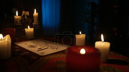 Photo for Magical session scene. Close up shot of spiritual board game with alphabet and numbers laying on the table, many candles standing around in the room. Occult divination concept. - Royalty Free Image