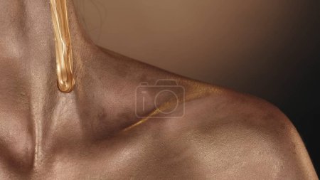 Photo for Close up shot of a female model shoulder and collarbone area covered with gold shimmer. Golden liquid paint flowing down by the the neck skin. Beauty skincare concept. - Royalty Free Image