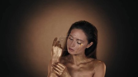 Photo for Portrait of an appealing woman. Close up shot of a female model with tears of golden paint taking off the dry paint from her skin. Creative advertisement concept. - Royalty Free Image